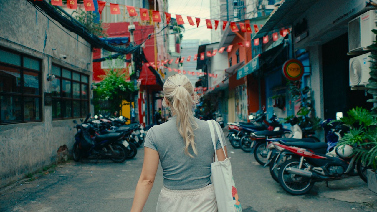 Documentary — a subject walking a flag-strung Saigon alley